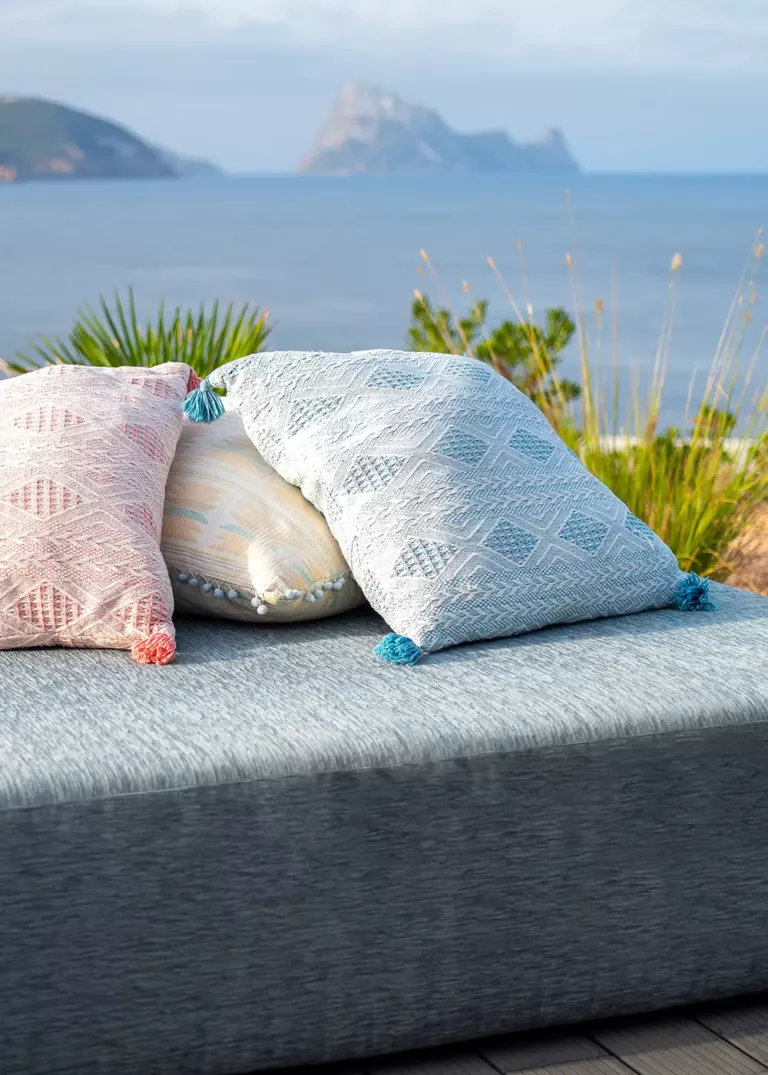 Entspannte Outdoor-Liege im 7Pines Resort Ibiza mit dekorativen Kissen und Blick auf das Meer und die Felseninsel Es Vedrà